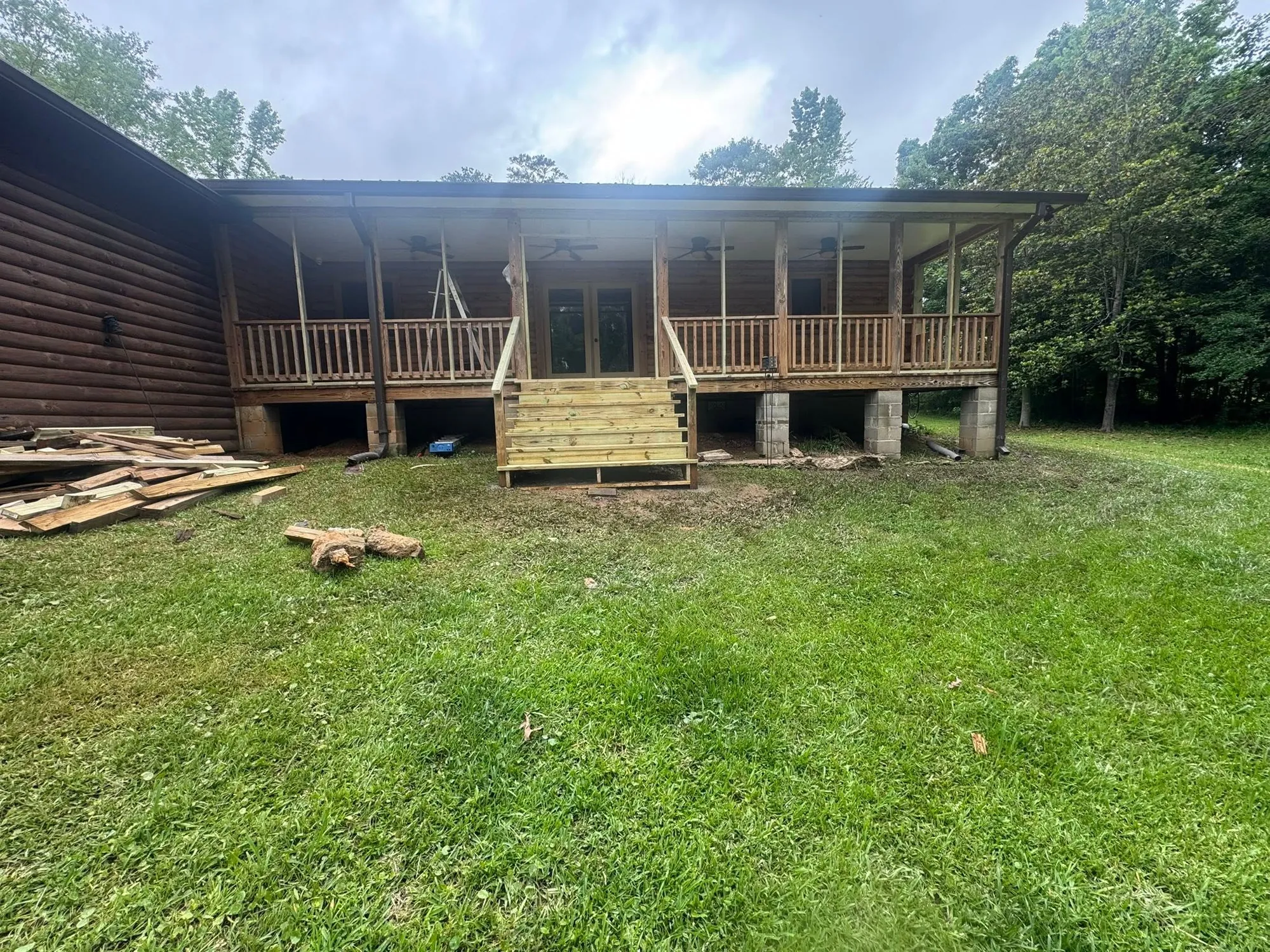 Wood-sided home with a freshly built back deck and porch roof over a green lawn